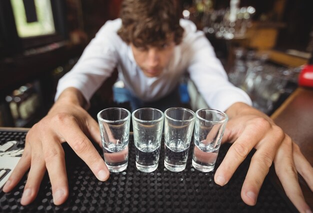 Camarero preparando y forrando vasos de chupito para bebidas alcohólicas en barra de bar