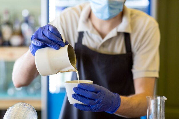 Camarero de primer plano con guantes preparando café