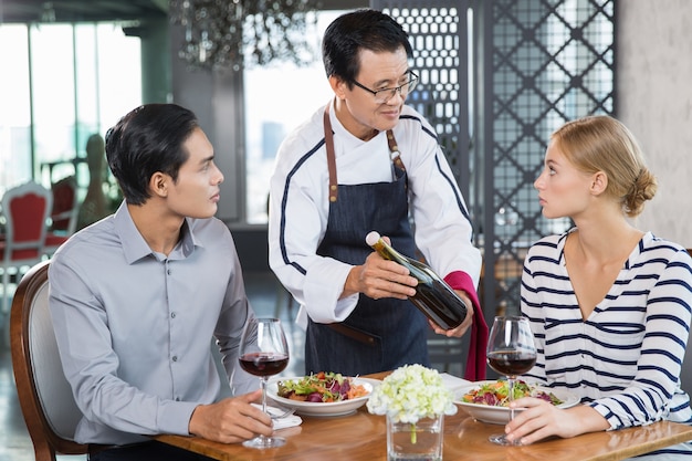 Camarero en el restaurante que ofrece el vino a Pareja joven