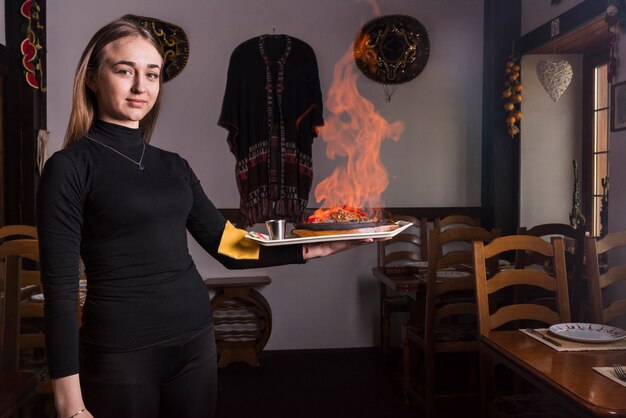 Camarero de sexo femenino que lleva la carne ardiente en restaurante