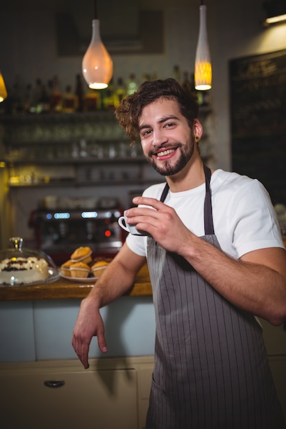 camarero sonriente con una taza de café en el mostrador de cafetería ©