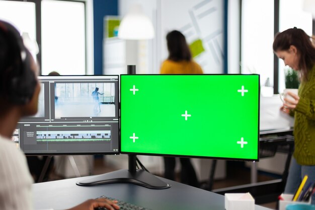 Camarógrafo de mujer africana con montaje de película de procesamiento de auriculares trabajando en pantalla verde, pantalla aislada chroma key de la computadora