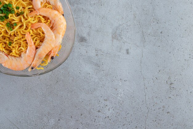Camarones y fideos en un plato de cristal, sobre el fondo de mármol.