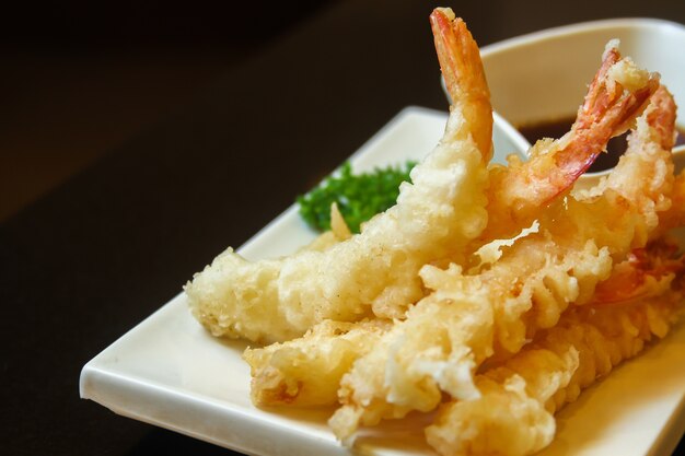 Camarones fritos con guarnición de verduras y salsa servidos en una bandeja plana blanca