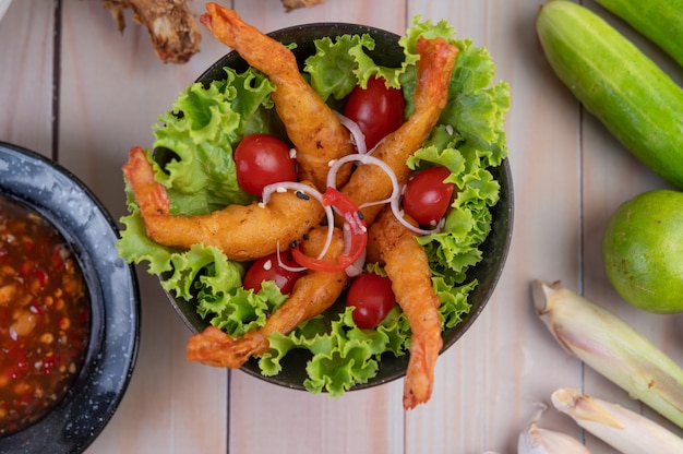 Camarones fritos rebozados en ensalada y tomates en un tazón de madera.