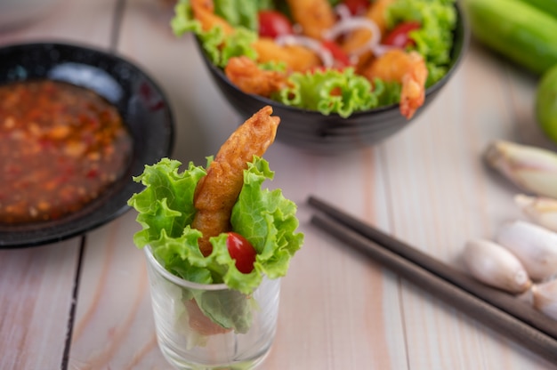 Camarones fritos rebozados en ensalada y tomates en un tazón de madera.