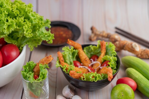 Camarones fritos rebozados en ensalada y tomates en un tazón de madera.