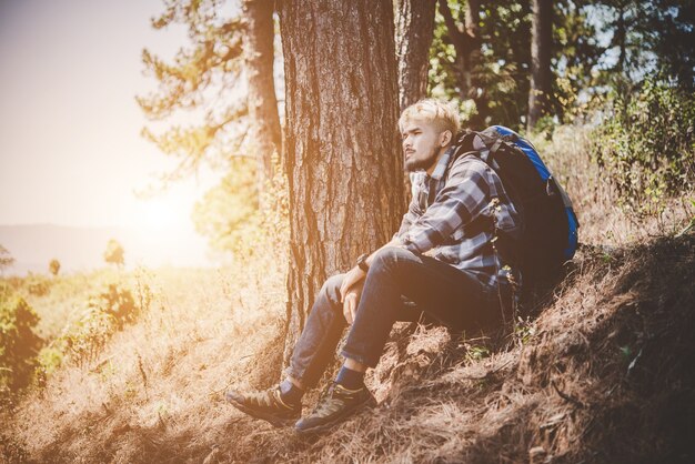 Caminante cansado joven con la mochila que se sienta en la tapa de la montaña mientras que se reclina después de caminata activa.