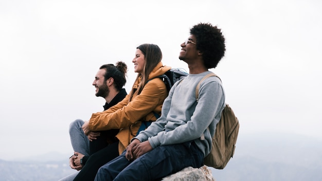 Caminante masculino y femenino feliz joven que se sienta en roca contra el cielo