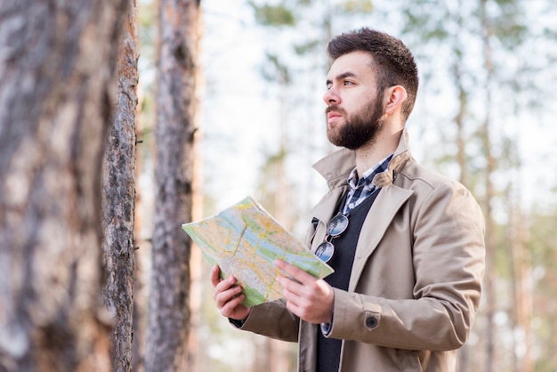 Caminante masculino joven que se coloca en el bosque que sostiene el mapa disponible