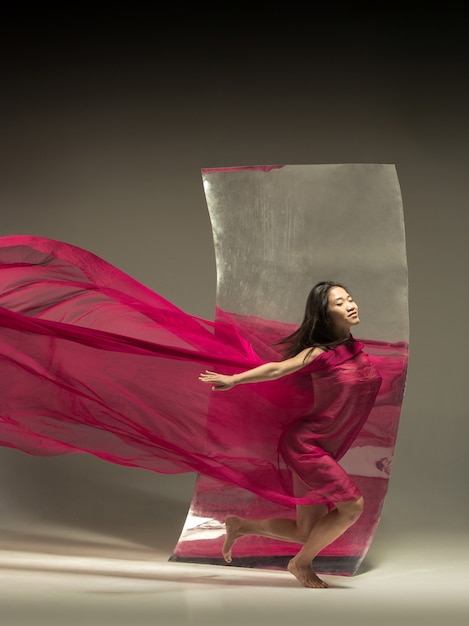 Camino al ideal. Bailarina de ballet moderno en pared marrón con espejo. Reflejos de ilusión en la superficie. Magia de flexibilidad, movimiento con tela. Concepto de baile de arte creativo, acción, inspirador.