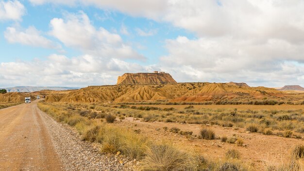 Camino en un desierto con una vista de un monolito bajo un cielo nublado