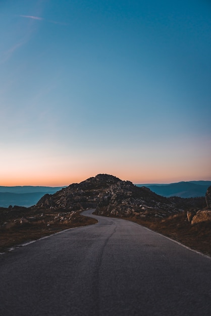 Camino estrecho que conduce a una cueva rocosa bajo el hermoso cielo del atardecer