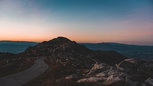 Camino estrecho que conduce a una cueva rocosa bajo el hermoso cielo del atardecer