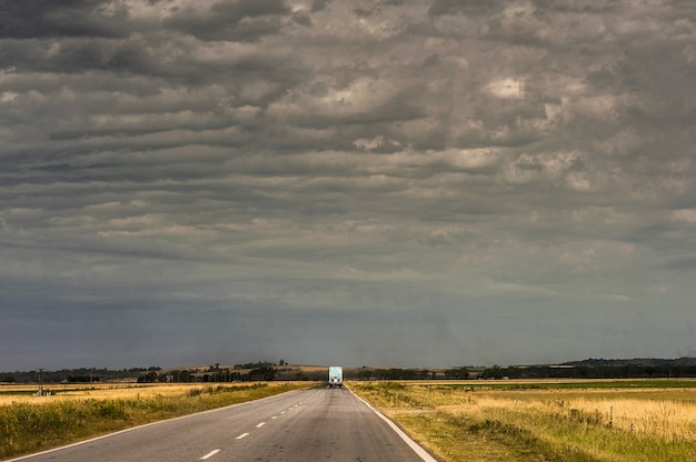 Camión en la carretera rodeado de campos vacíos bajo el cielo nublado