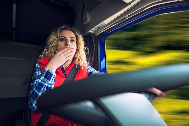 Camionero mujer bostezo debido al cansancio y el aburrimiento mientras conduce el camión