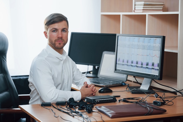 Camisa blanca y muchos dispositivos. El examinador de polígrafo trabaja en la oficina con el equipo de su detector de mentiras