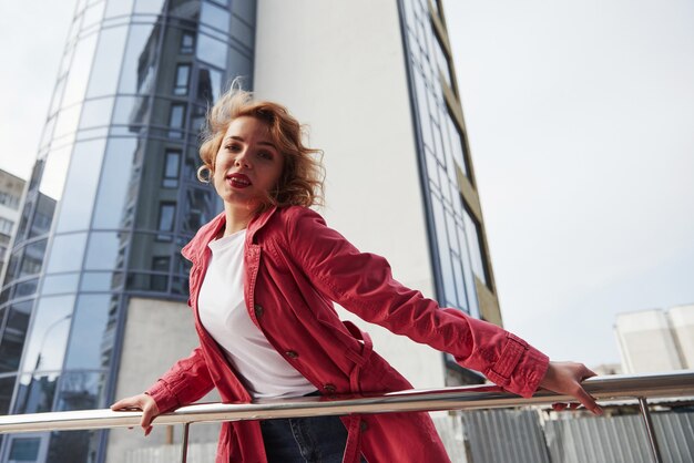 En camisa blanca. Mujer bonita adulta en abrigo rojo cálido tiene caminar en la ciudad en su tiempo de los fines de semana