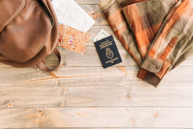 Camisa a cuadros; bolso; mapa; Pasaporte y moneda sobre fondo de madera.