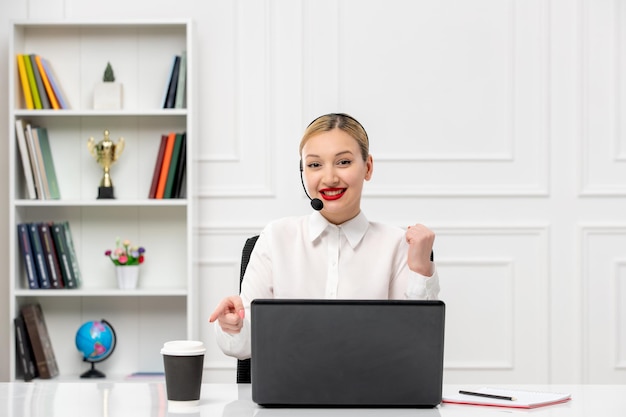 Camisa de oficina de linda chica rubia de servicio al cliente con auriculares y computadora levantando los puños