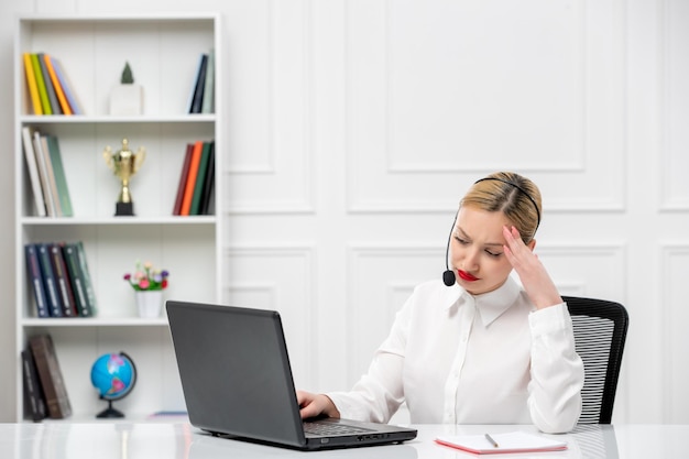 Camisa de oficina de linda chica rubia de servicio al cliente con auriculares y computadora tocando la cabeza cansada