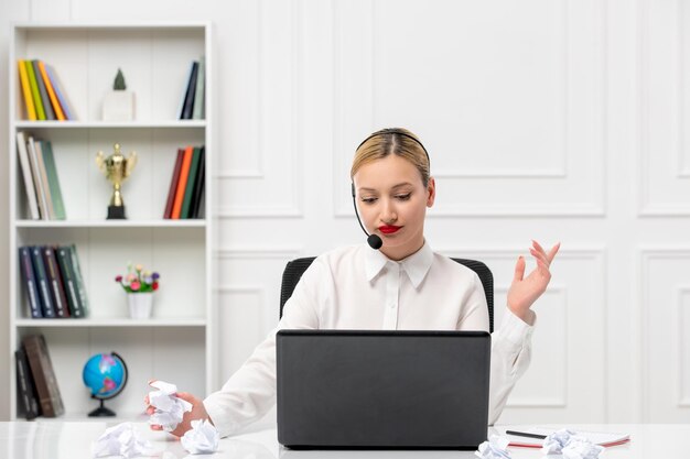 Camisa de oficina de linda chica rubia de servicio al cliente con auriculares y pensamiento de computadora