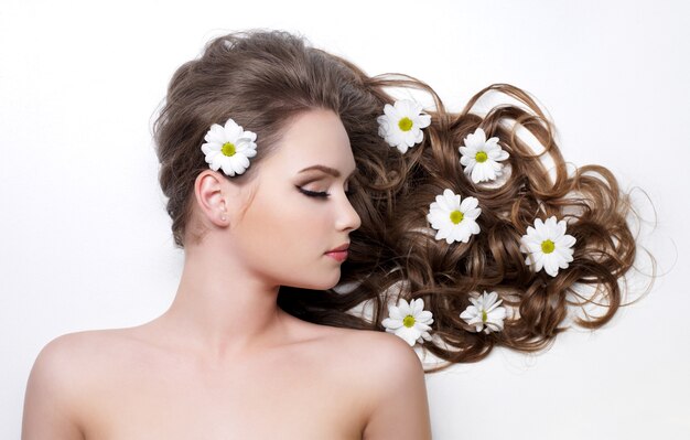 Camomiles en hermoso hermoso cabello largo y rizado de mujer joven - espacio en blanco