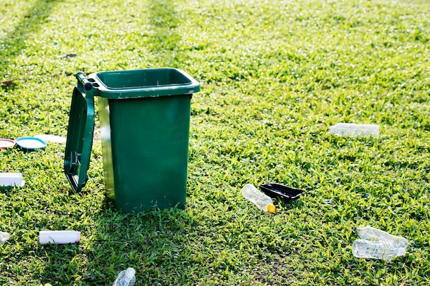 Campaña de reciclaje con papelera verde y botellas de plástico desperdiciadas en el campo