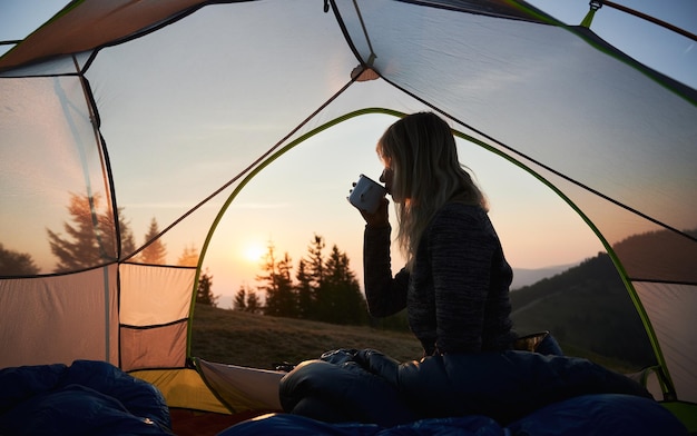 Campista femenina dando la bienvenida a la mañana fresca y soleada en la montaña