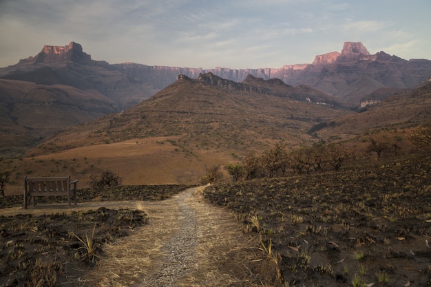 Campo de hierba seca quemada en el desierto con un camino estrecho y hermosas montañas rocosas