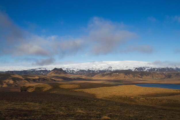 Campo rodeado de agua y colinas cubiertas de nieve bajo un cielo nublado en Islandia
