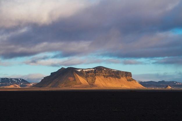 Campo rodeado de rocas cubiertas de nieve bajo un cielo nublado durante la puesta de sol en Islandia