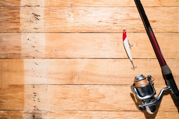Caña de pescar con cebo de pesca rojo y blanco en tablón de madera