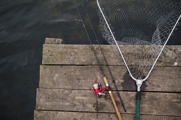 Foto gratuita caña de pescar y red de pesca en el borde del muelle de madera sobre el lago