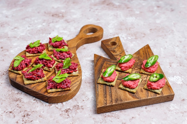 Canapés de humus de remolacha con rodajas de pimiento verde y perejil en la tabla de cortar sobre una superficie clara