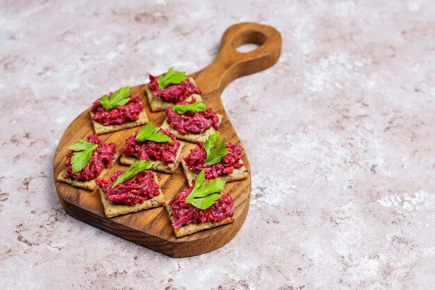 Canapés de humus de remolacha con rodajas de pimiento verde y perejil en la tabla de cortar sobre una superficie clara