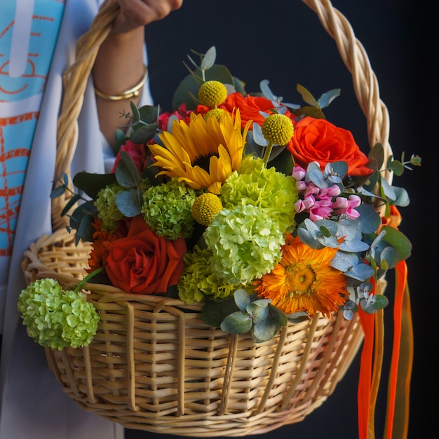 Una canasta de bambú con girasoles, rosas rojas y claveles.