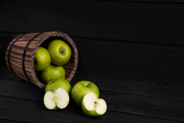 Una canasta de madera llena de manzanas verdes maduras colocadas sobre una mesa de madera oscura. Foto de alta calidad