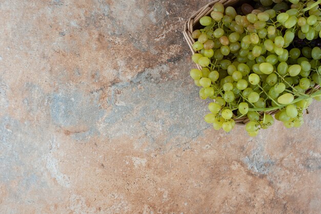 Foto gratuita una canasta de mimbre llena de uvas dulces en la mesa de mármol.