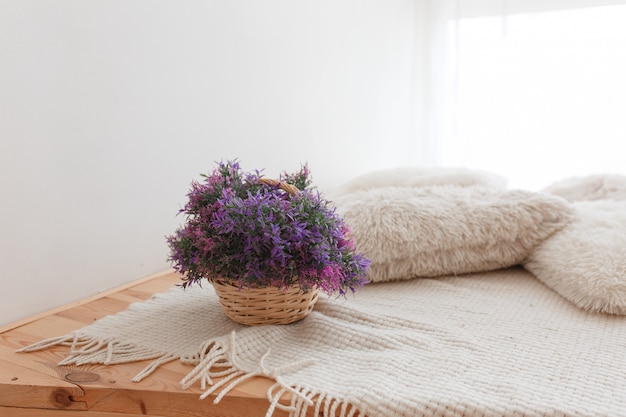 Canasta de yute con flores de color púrpura, piso de madera con almohadas de punto y cubierta.