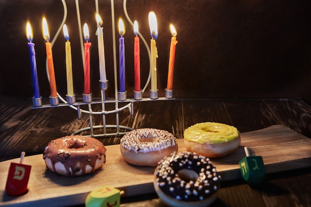 Candelabro judío tradicional de hanukkah feliz con velas, donas y peonzas en madera marrón ...