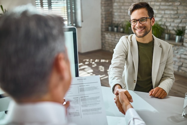 Candidato masculino feliz saludando a un miembro del equipo de recursos humanos en una entrevista de trabajo en la oficina