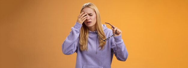 Cansada, mareada, linda chica rubia quitándose las gafas tocando la frente, se siente enferma y sufre dolor de cabeza