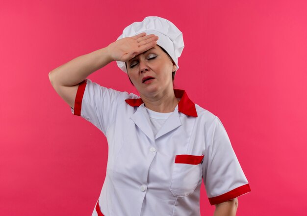 Cansado cocinero de mediana edad en uniforme de chef poniendo la mano en la frente