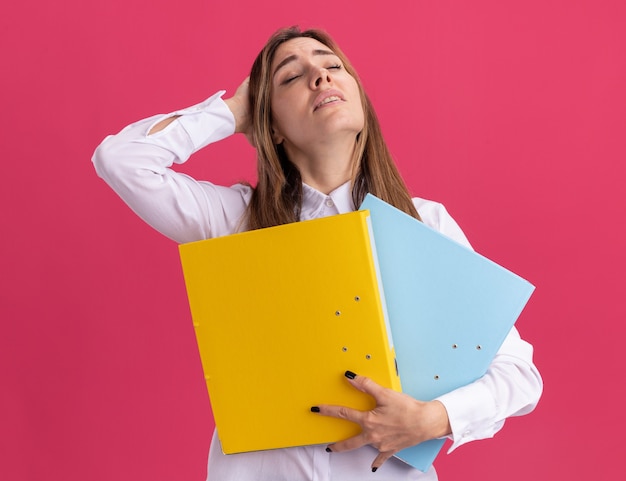 Cansado joven bastante caucásica pone la mano en la cabeza y sostiene carpetas de archivos