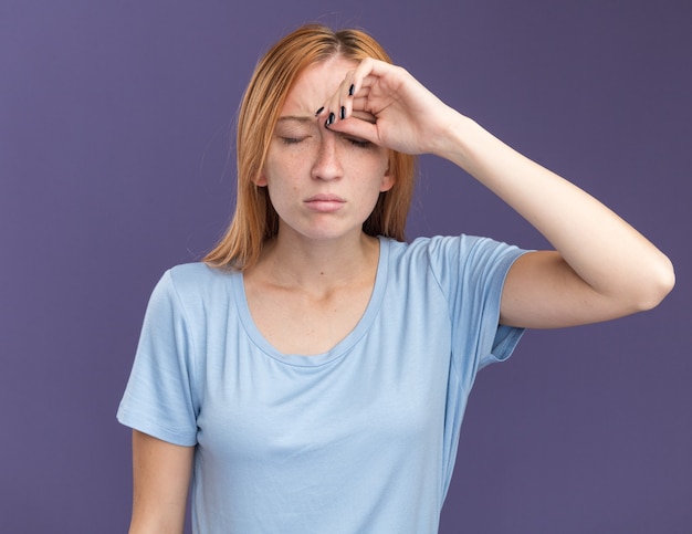 Foto gratuita cansado joven pelirroja pelirroja con pecas pone la mano en la frente aislada en la pared púrpura con espacio de copia