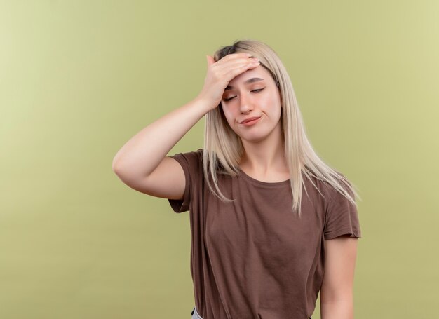 Cansado joven rubia poniendo la mano en la frente con los ojos cerrados en la pared verde aislada con espacio de copia