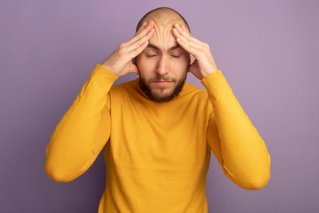 Cansado con los ojos cerrados joven guapo poniendo las manos en la frente aislada en la pared púrpura