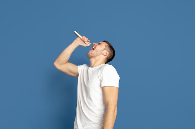 Cantando como celebridades, estrellas. Retrato de hombre joven caucásico sobre fondo azul.