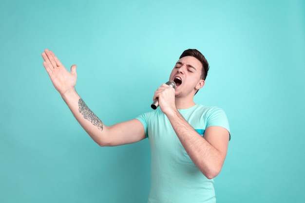 Foto gratuita cantando como una estrella. retrato de joven caucásico aislado en la pared azul del estudio